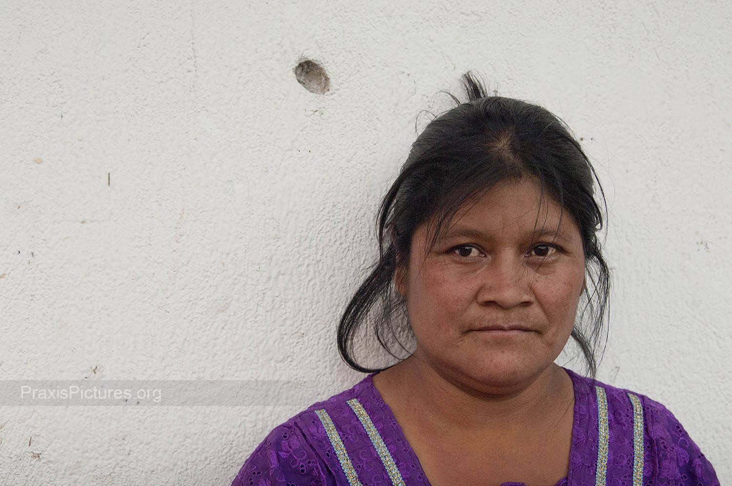 CALENDARIA - Candelaria stands outside her home directly below the mine in front of a bullet hole in her wall. Candelaria’s husband is currently working at a hotel for tourists in Cancun, Mexico, so that he can send money back for his family, who also lost some of its farm land to the road expansion. One night while the family was asleep, a vehicle drove past her home, and someone fired four gun shots at Candelaria’s house. “Before we all lived peacefully,” says Candelaria’s brother-in-law Victor, “one heard about violence, but in the capital, now the violence is here, among us—to the point of parents fighting with their children and brothers fighting each other. We are very worried, because we hear people saying: ‘we will kill or kidnap those who are against mining,’ and there are many killings and kidnappings, not only here but also in many other villages above the mine. We are living a life that is very difficult, and it will continue to get worse. And I think: who will defend us? What will we do?”