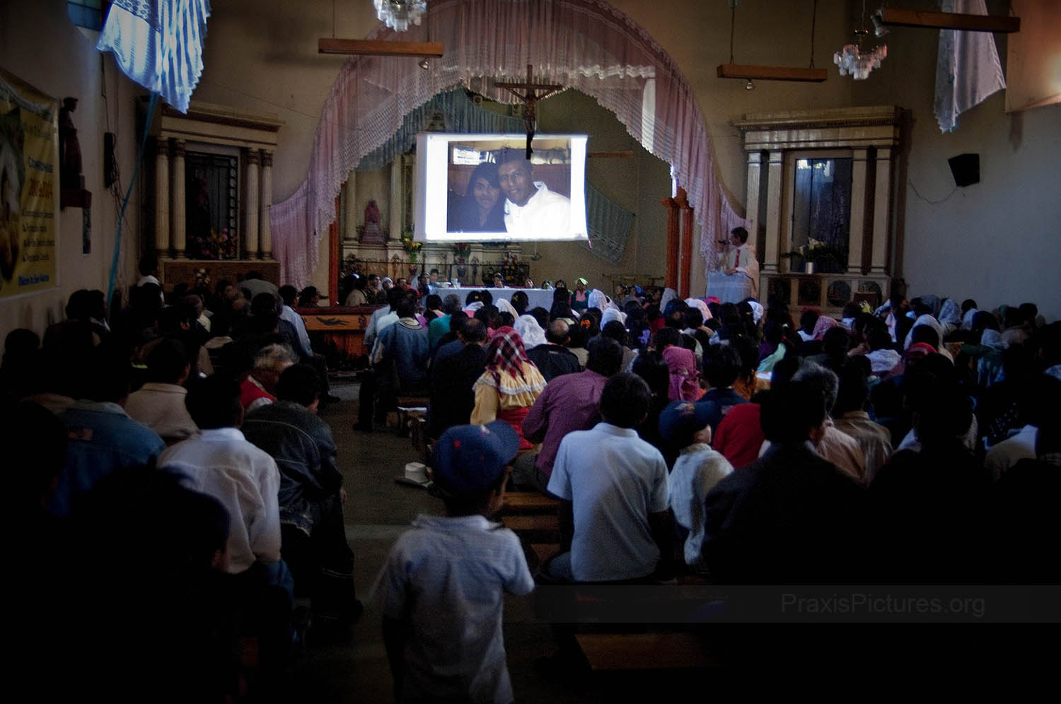 MISSING FAMILY - Community members of San Miguel Ixtahuacán gather inside their Church to see pictures from Father Erick’s recent trip to the USA. Father Erick’s trip included several cities accross the United States, so that he could visit peoples’ relatives who are working there, often undocumented, in order to support their families. “They said that we would benefit by getting jobs,” someone murmurs in the crowd, “so where are the jobs? If there are jobs here, why do so many of us have to leave our families and homes risking our lives for a few coins?” In addition to the United States, many people also emigrate to Mexico or to the coastal regions of Guatemala to work in the sugar plantations.