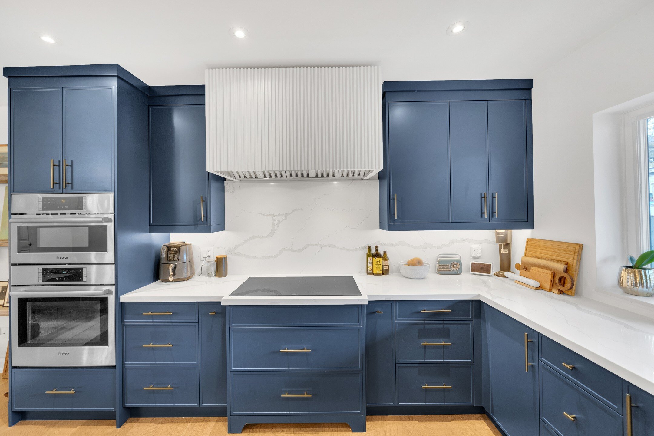 This kitchen in the Beaches, a prime Toronto neighborhood, showcases a modern yet classic design with deep blue cabinets, white marble-like countertops, and stainless steel appliances. The mix of metals using satin brass hardware adds a warmth. The d