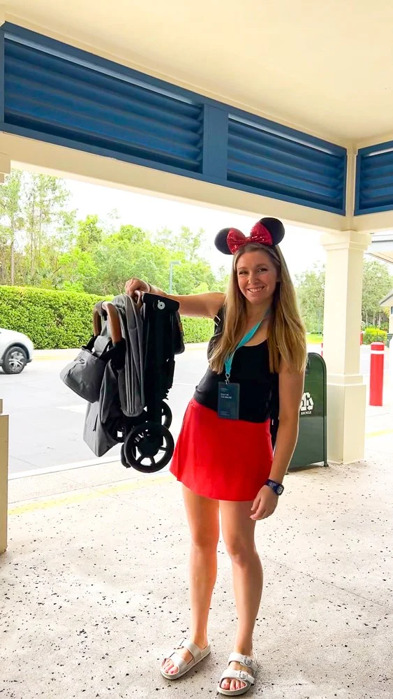 mom holding stroller in red skort and black tank top and mouse ears