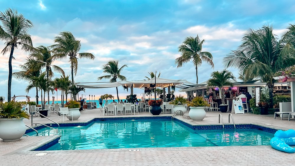 hotel pool with palm trees outdoor restaurant and ocean behind it