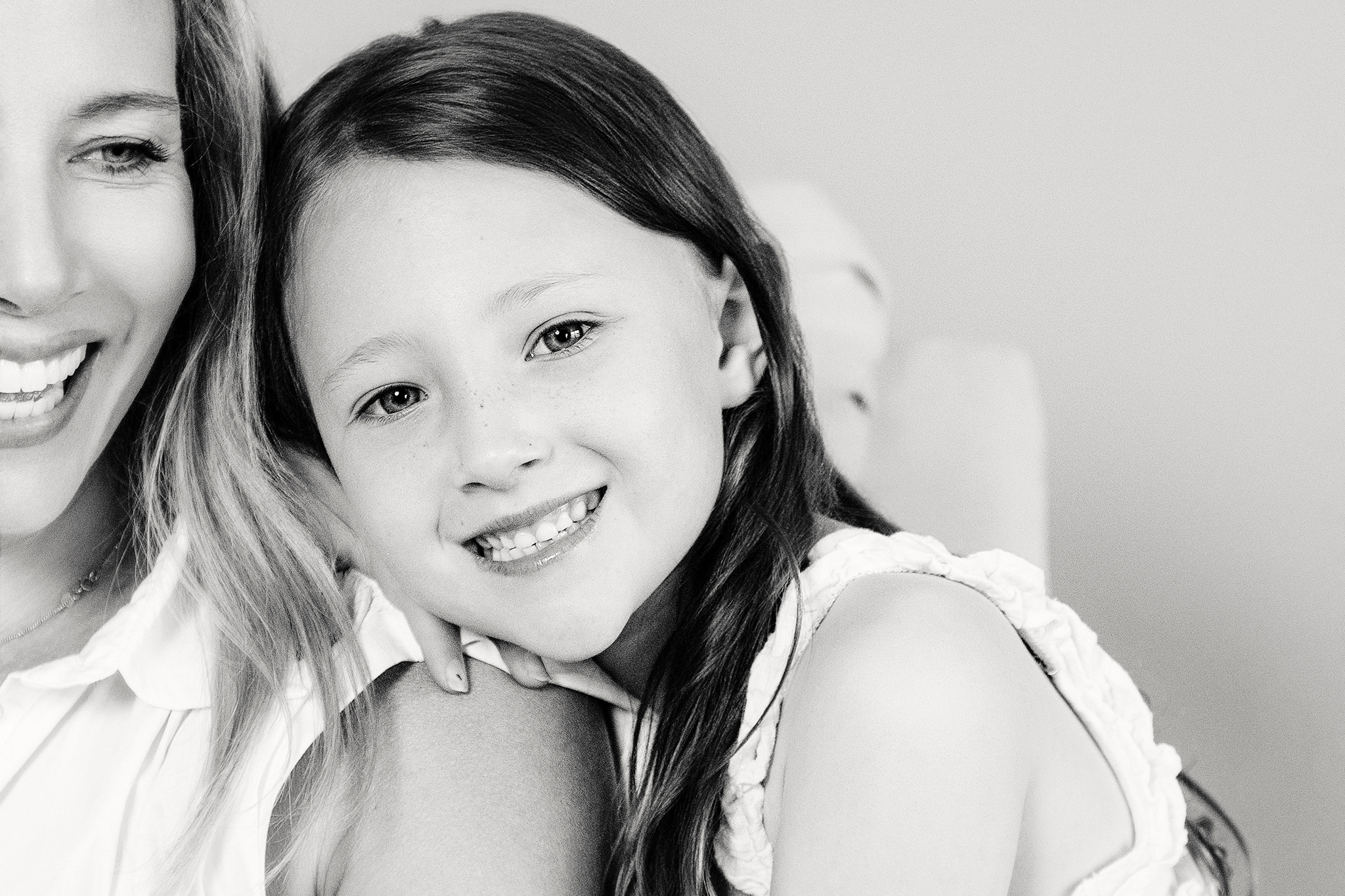 A black-and-white photo of a woman and a young girl smiling together during a studio mommy and me mini session in Northville, Michigan. The woman is on the left side, and the girl is on the right, with their faces close together.