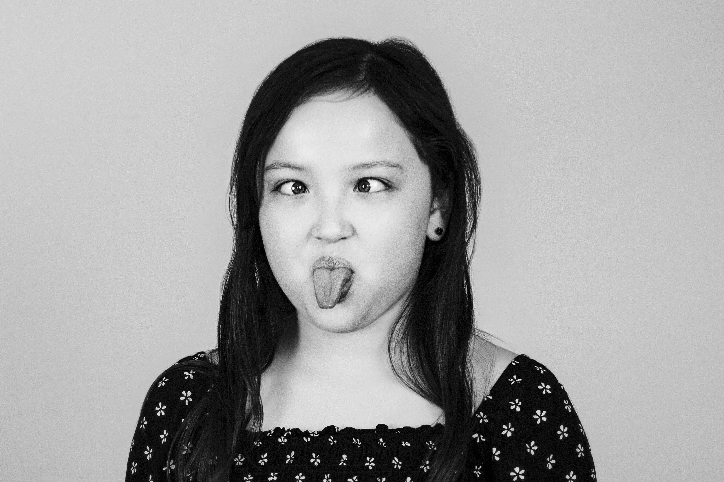Black and white photo of a girl with long dark hair, making a goofy face with her tongue sticking out.