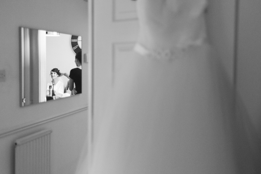 Bride getting ready reflected in mirror with wedding dress in foreground