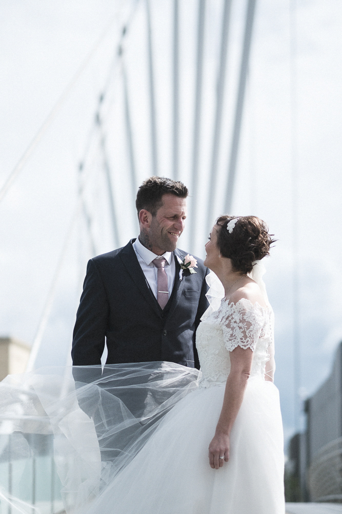 Bride and groom look lovingly at each other on Salford's Media City bridge