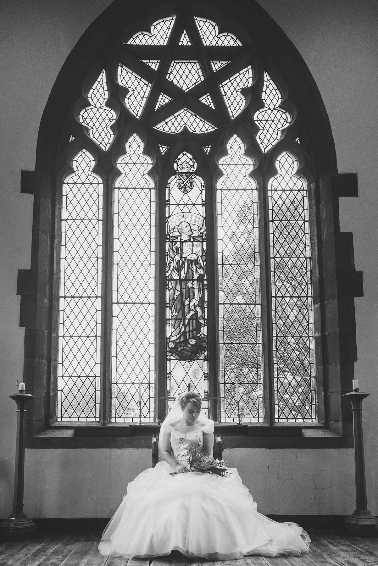 Bride looks at flowers underneath grand stain glass window