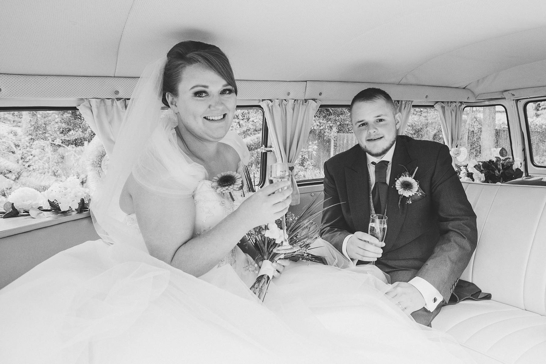 Bride and groom pose with drinks inside wedding campervan