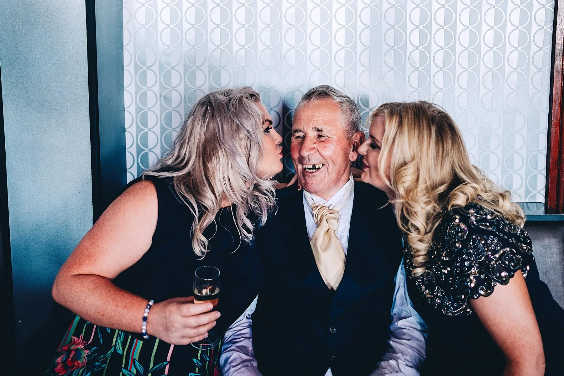 Old man laughs while two younger women kiss him