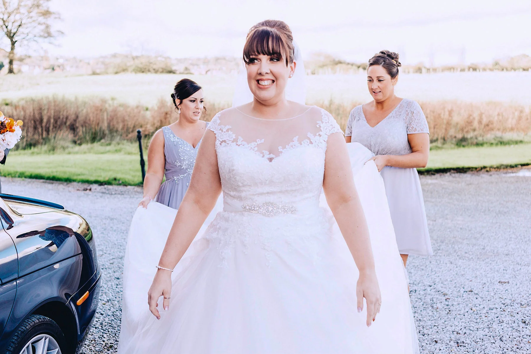 Bride looks happy while bridesmaids hold her dress