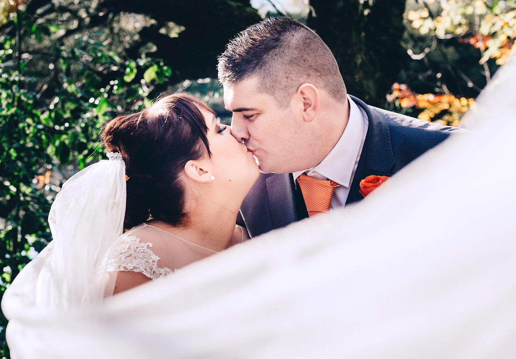 Bride and groom kiss while veil blows across them