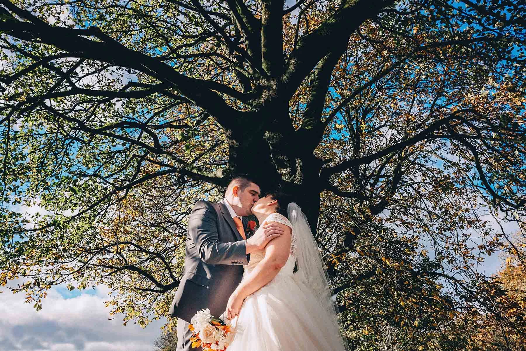 Bride and groom kiss underneath large tree