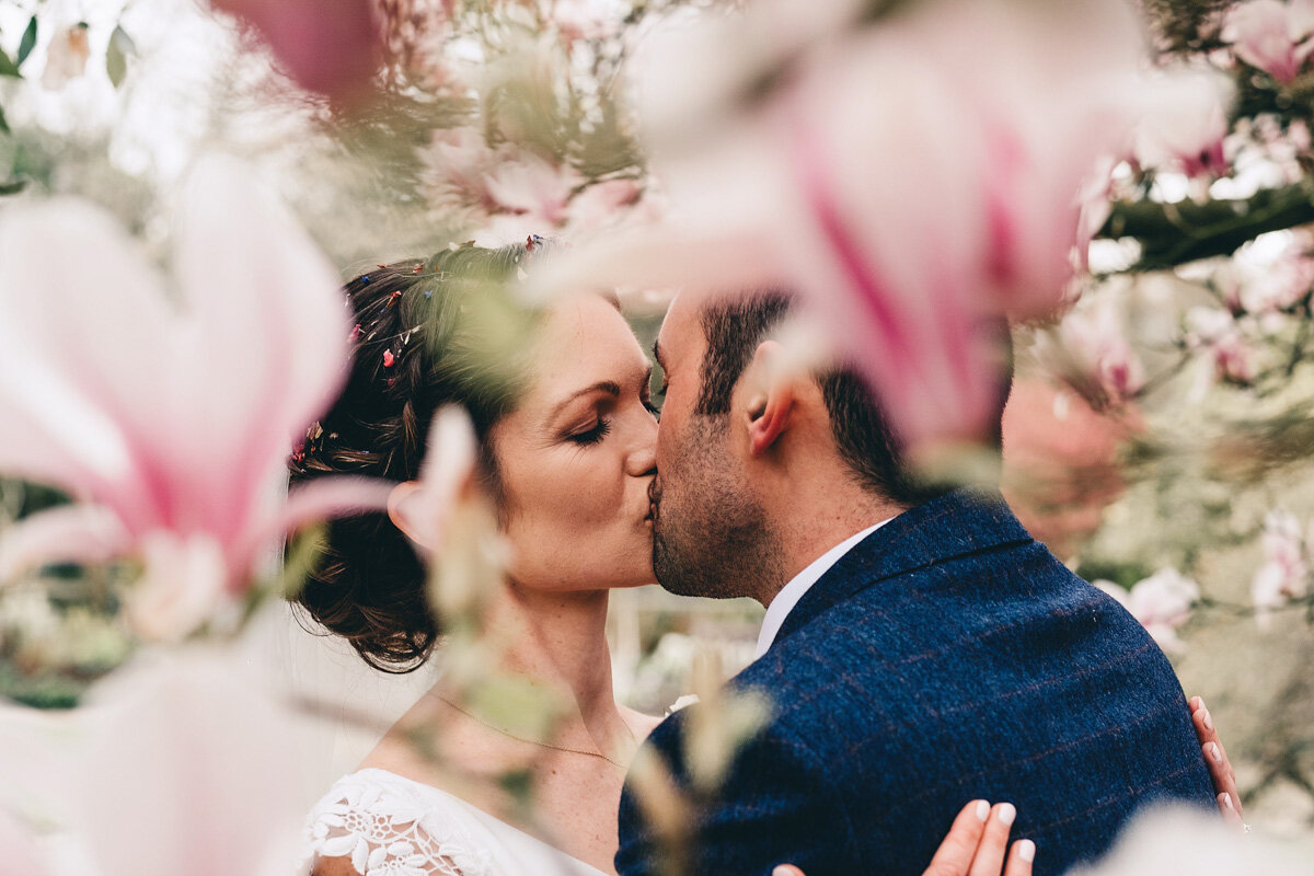 Bride and groom kiss in Didsbury Parsonage Gardens with flowers in full bloom