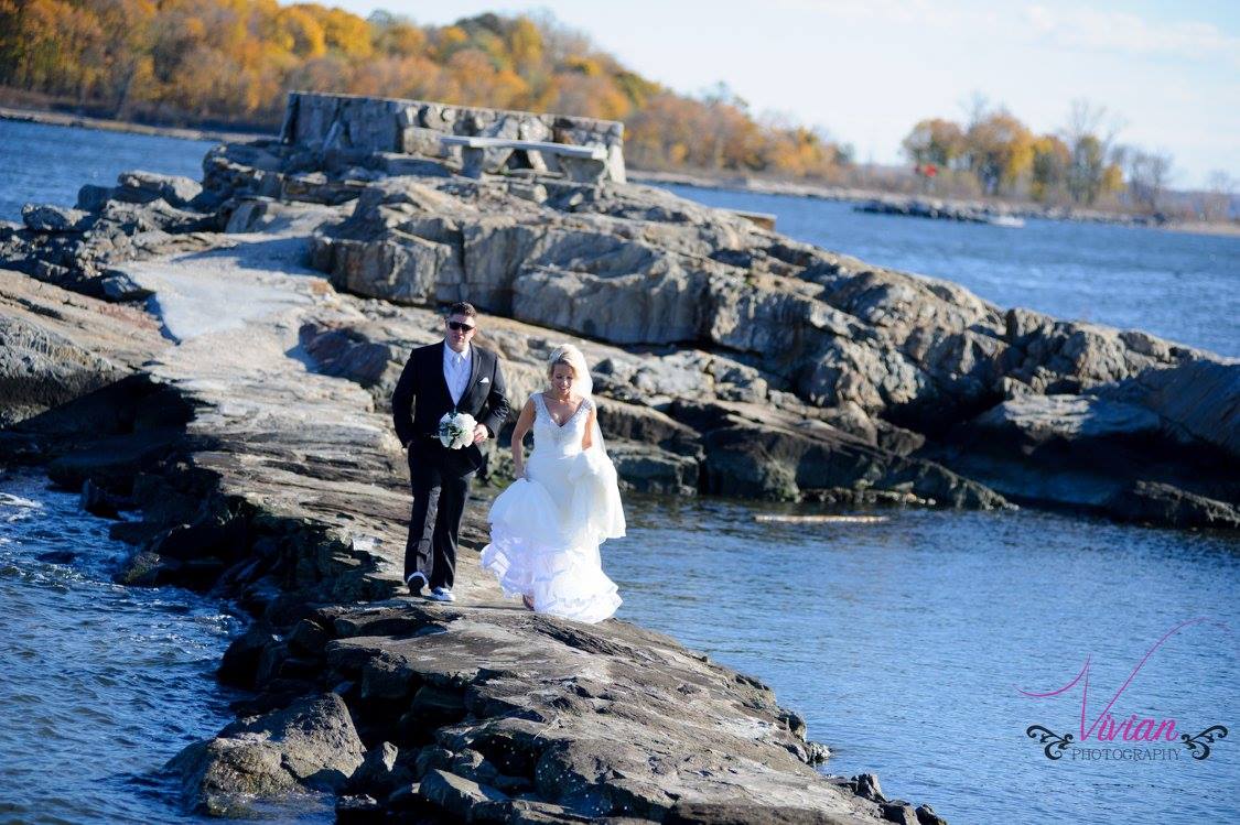 bride-and-groom-far-away-walking-towards-camera-on-rocks-over-body-of-water.jpg