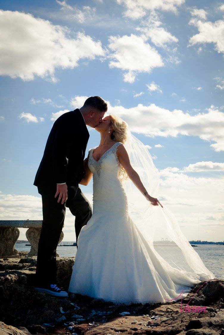 bride-and-groom-kissing-on-rocks-overlooking-water-with-blue-sky.jpg