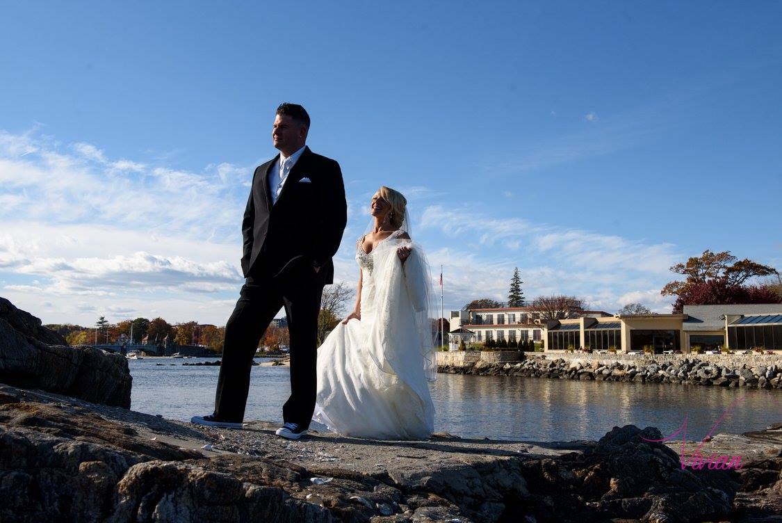 groom-looking-away-as-bride-approaches-from-behind-on-rocks-over-body-of-water.jpg