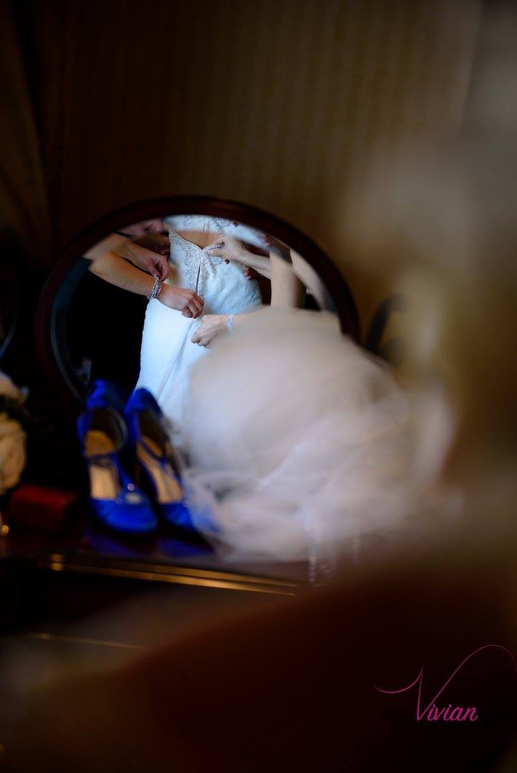 reflection-in-mirror-of-bridesmaids-zipping-brides-dress.jpg