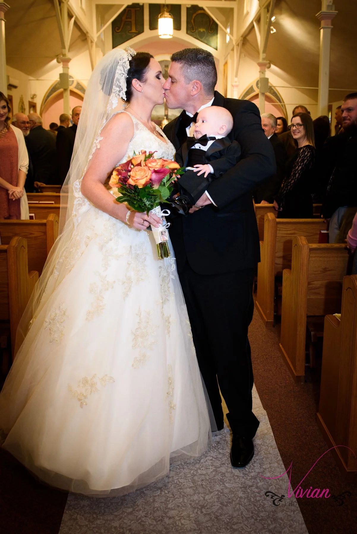 bride-groom-kissing-groom-holding-baby.jpg