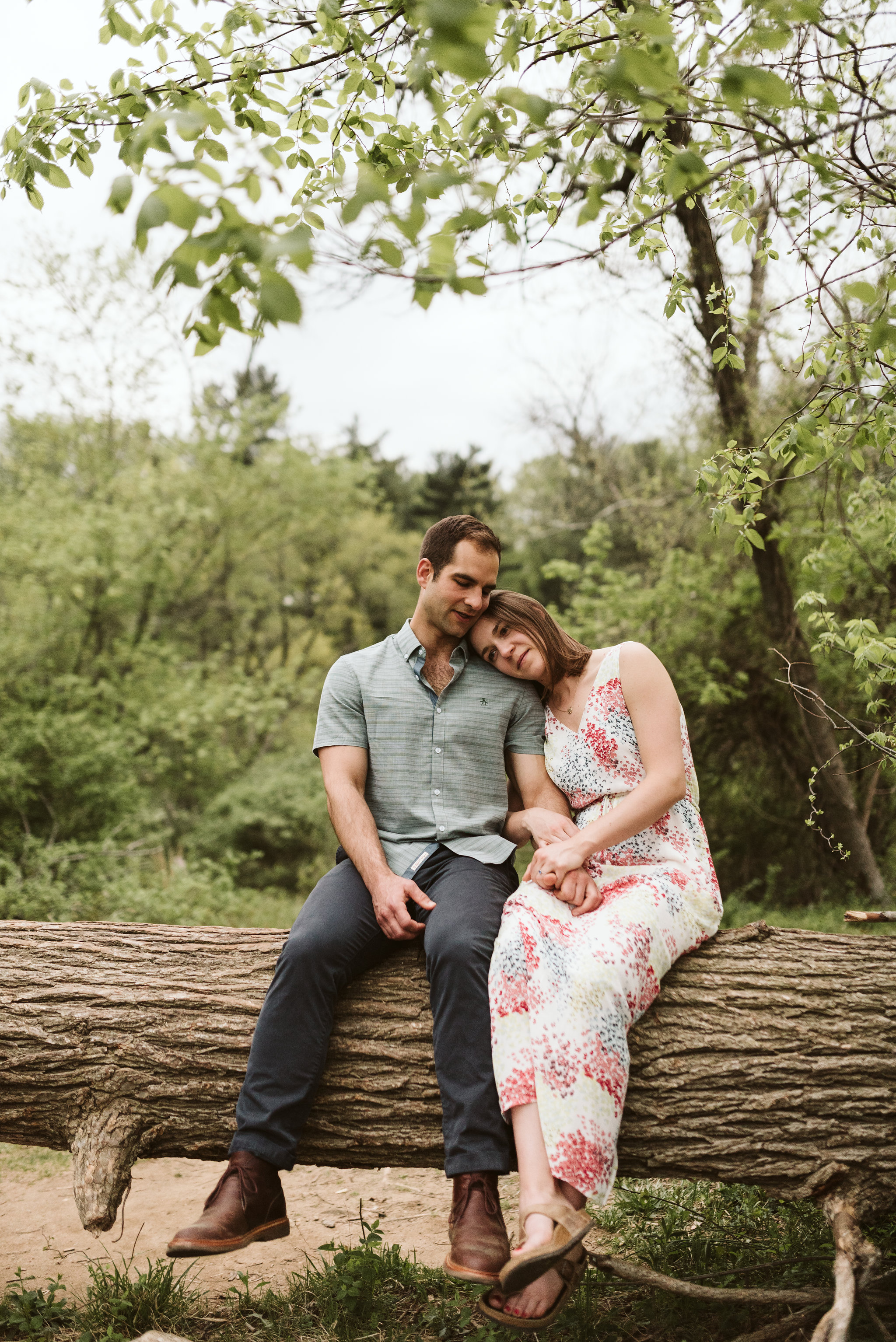 man and woman sitting on a log wearing long white dress and blue shirt for authentic engagement photos