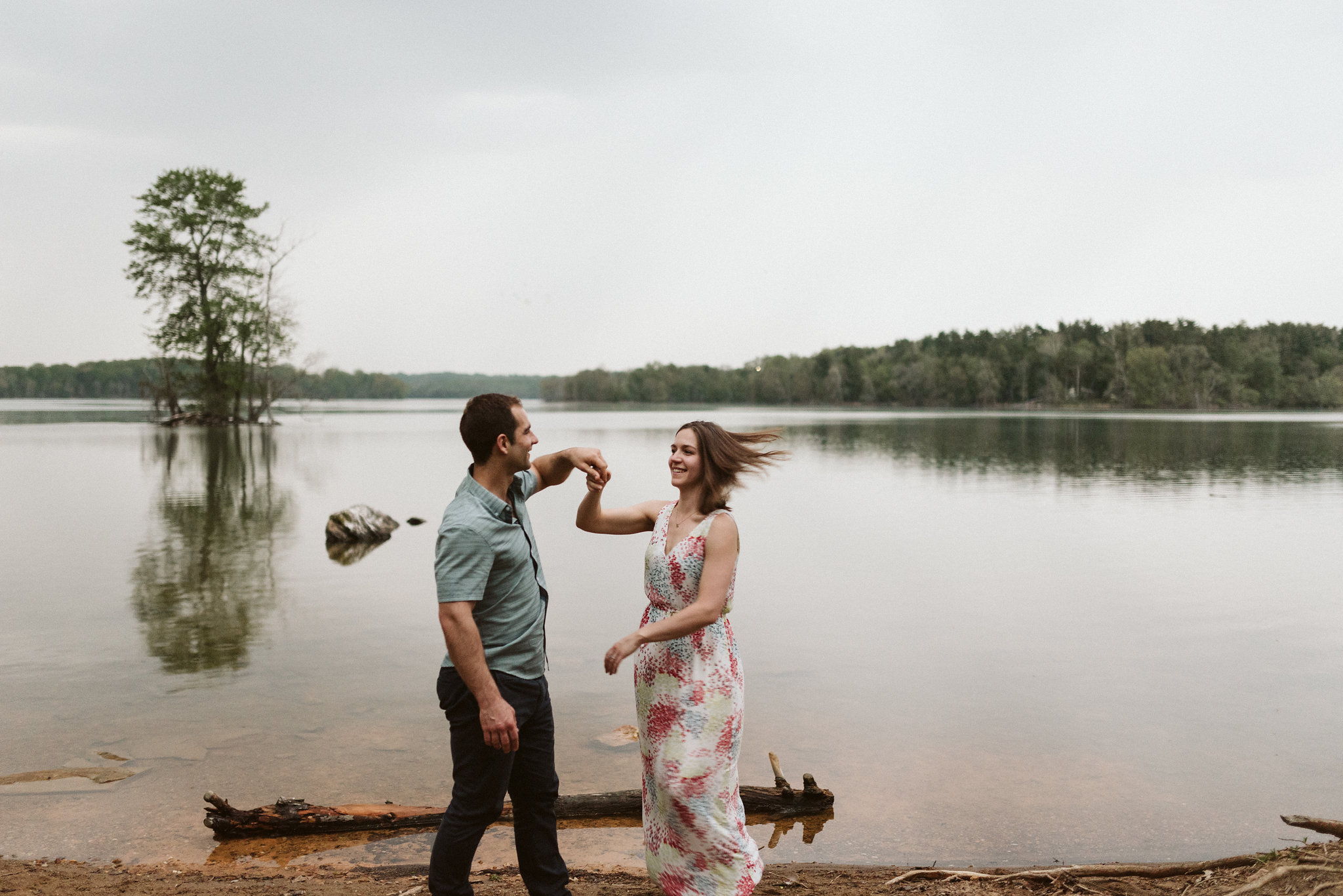 woman’s hair flowing while dancing with fiance in front of lake