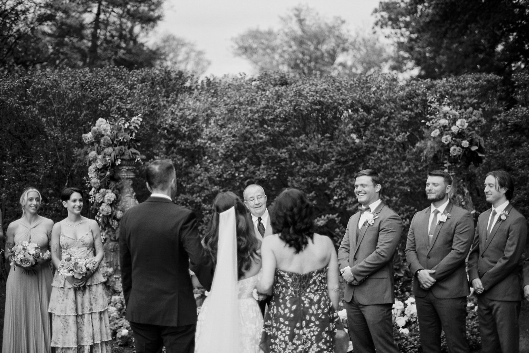 black and white photo of bride walking down the aisle on film with parents and groom is smiling