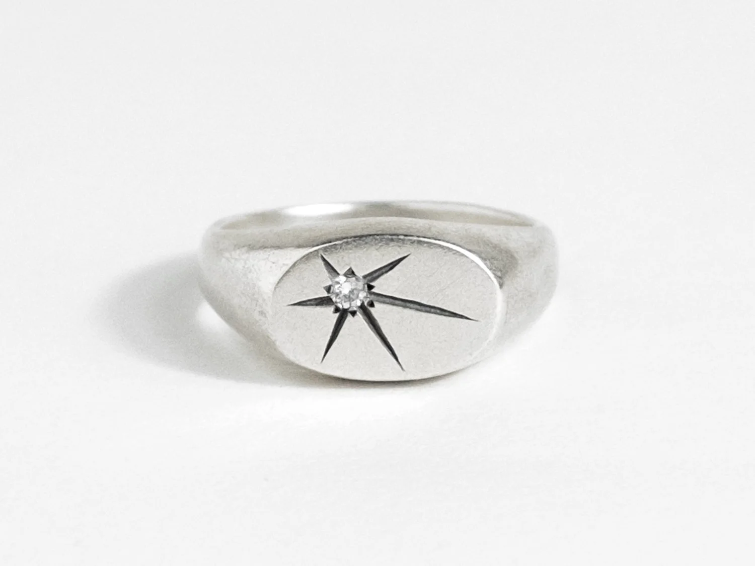 Wide silver signet ring with a single star-set diamond on the flat face
