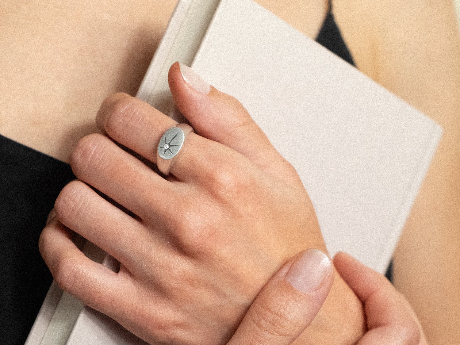 Model's hand wearing a silver signet ring with a single diamond set in a star shape