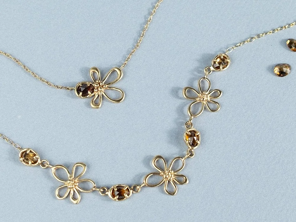 Pair of gold necklaces with flower shapes and gemstones along the center