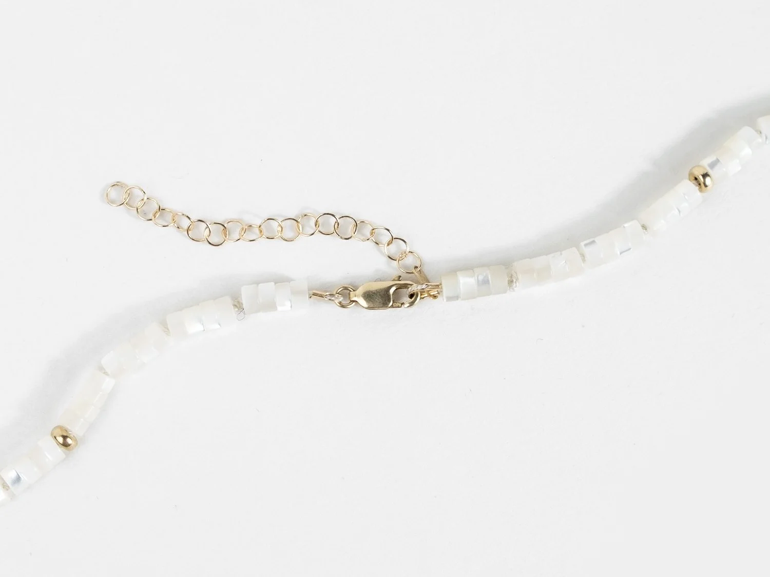 Detail of a gold lobster claw closure and extender chain on the end of a mother of pearl and gold bead necklace