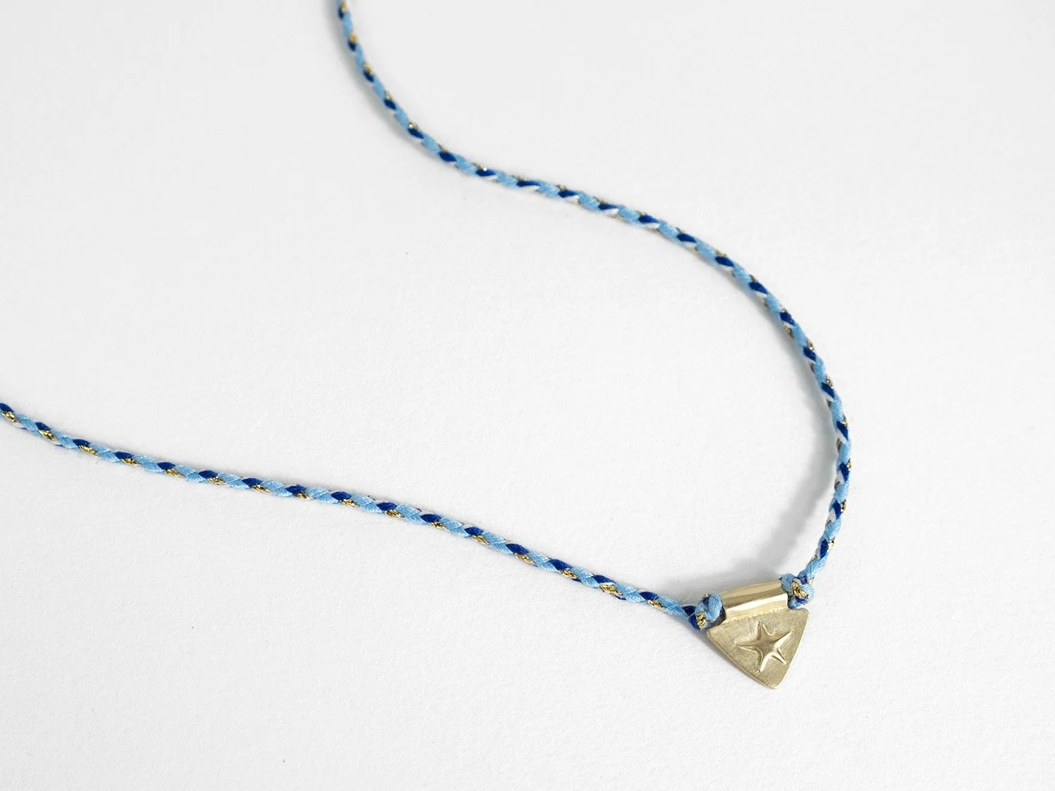 Triangle-shaped gold charm with a raised star motif on a braided cord necklace