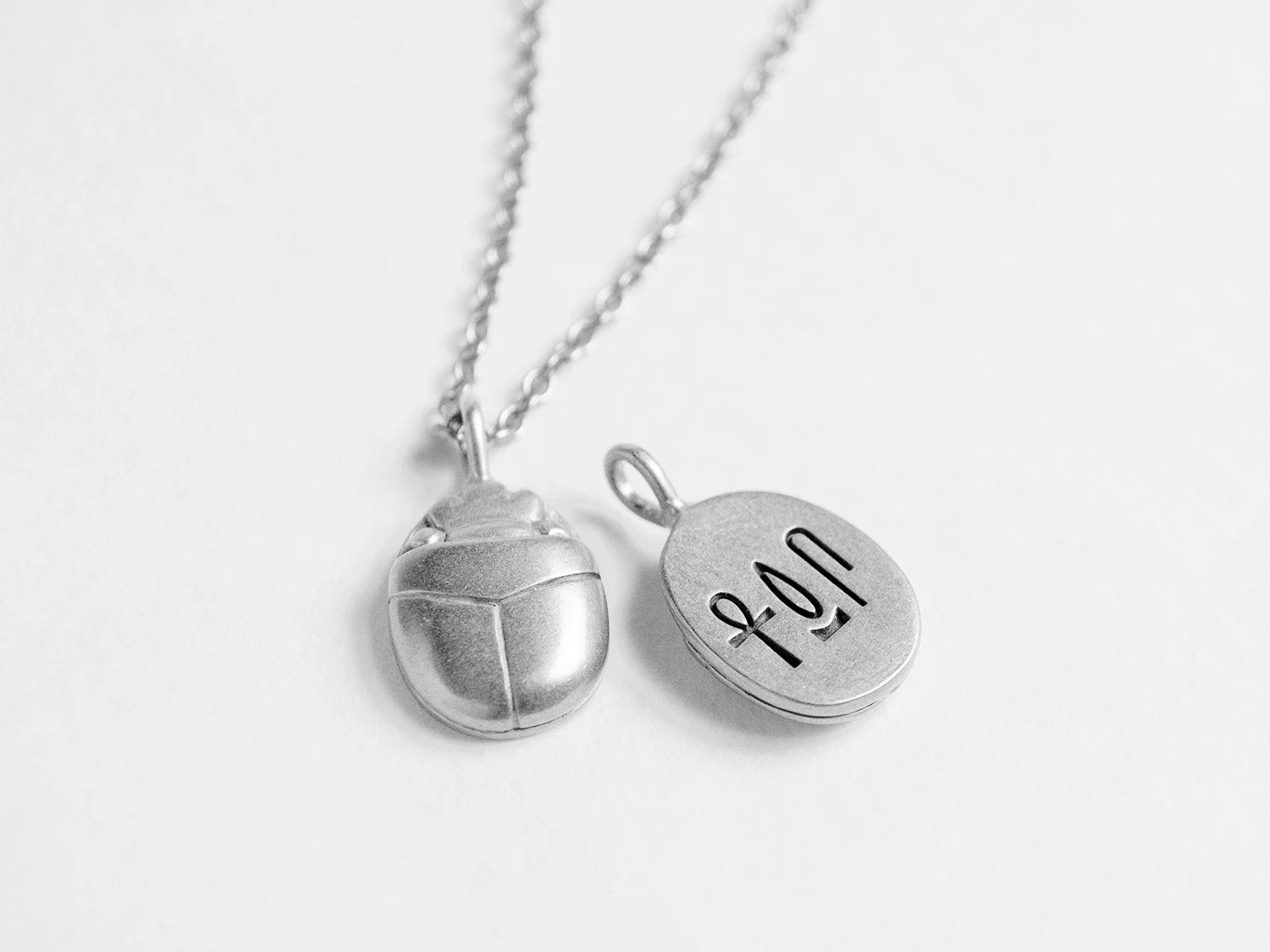 Silver pendant necklace in the shape of a scarab beetle with hieroglyphs carved into the back