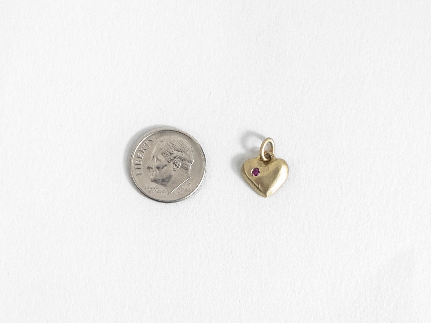 14k gold puffy heart charm with ruby next to a dime
