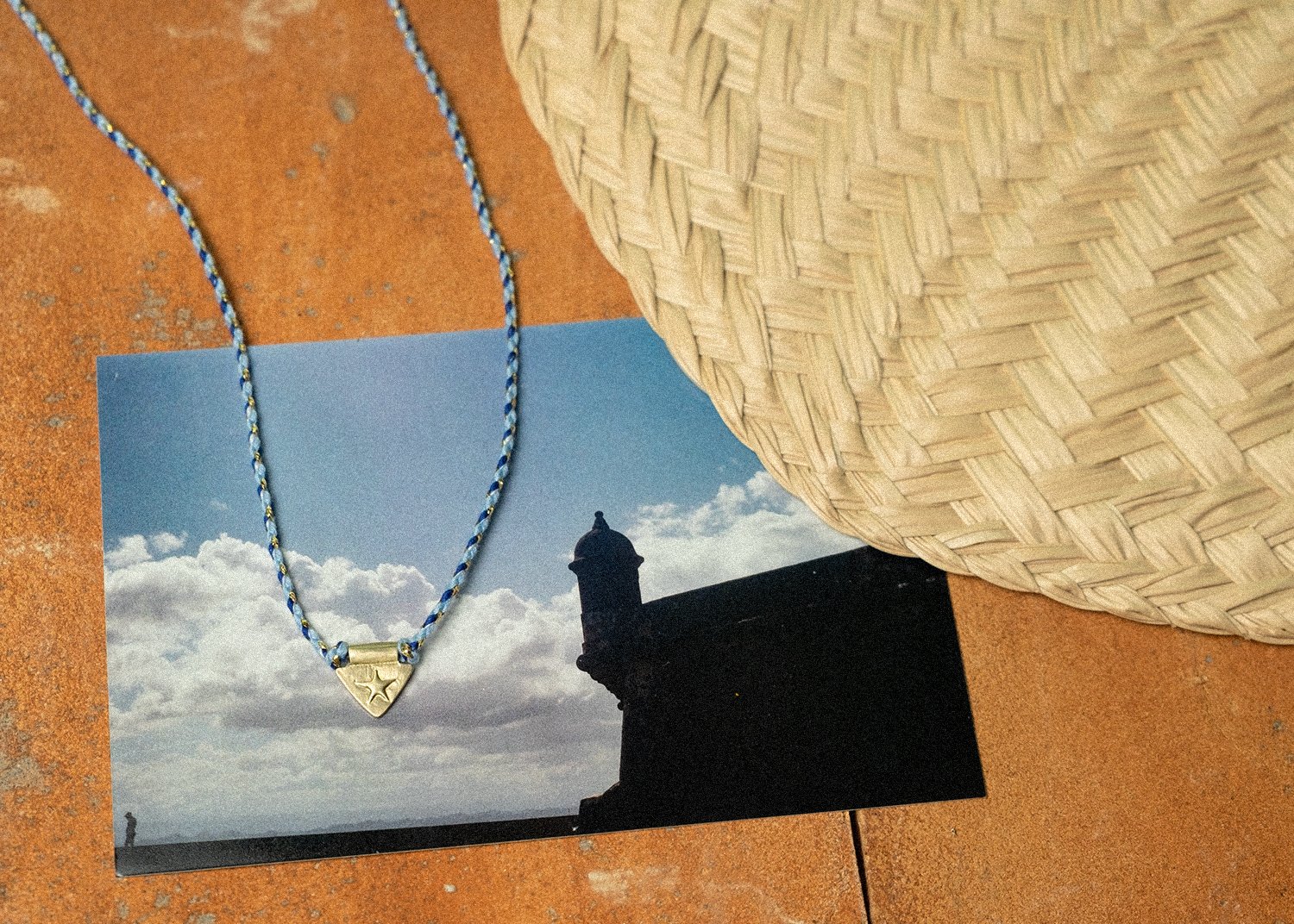 Gold charm necklace on a photograph of a monument next to a woven fan