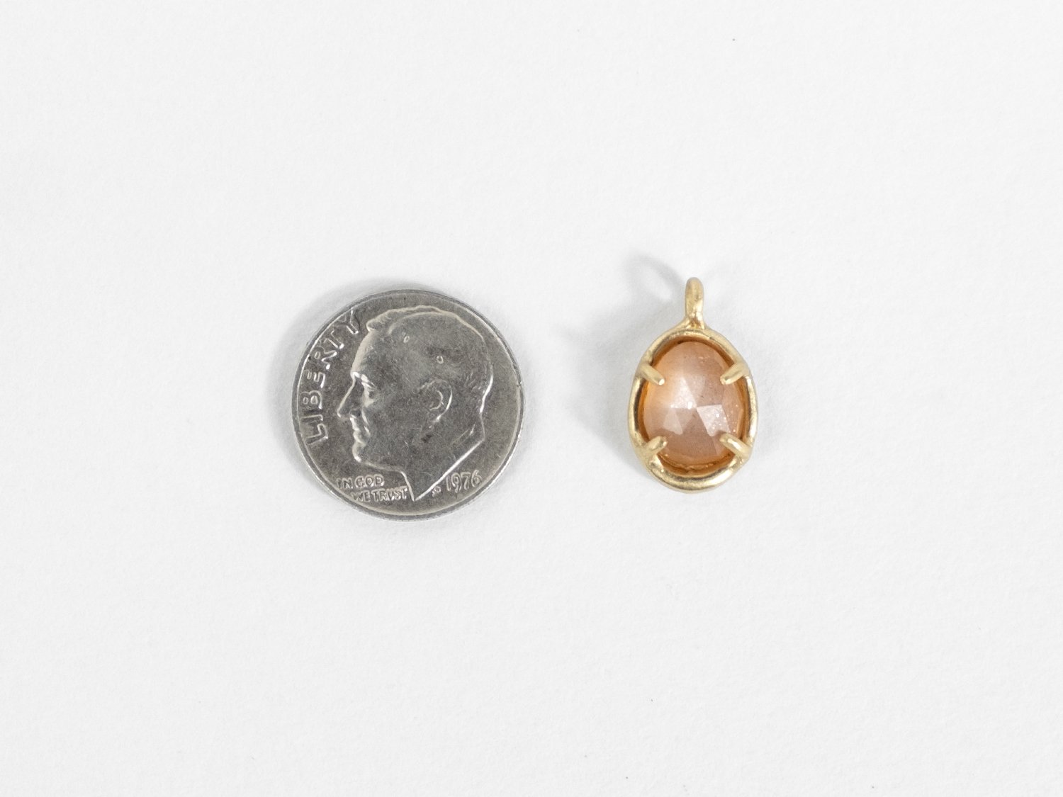 14k gold and peach moonstone charm next to a dime