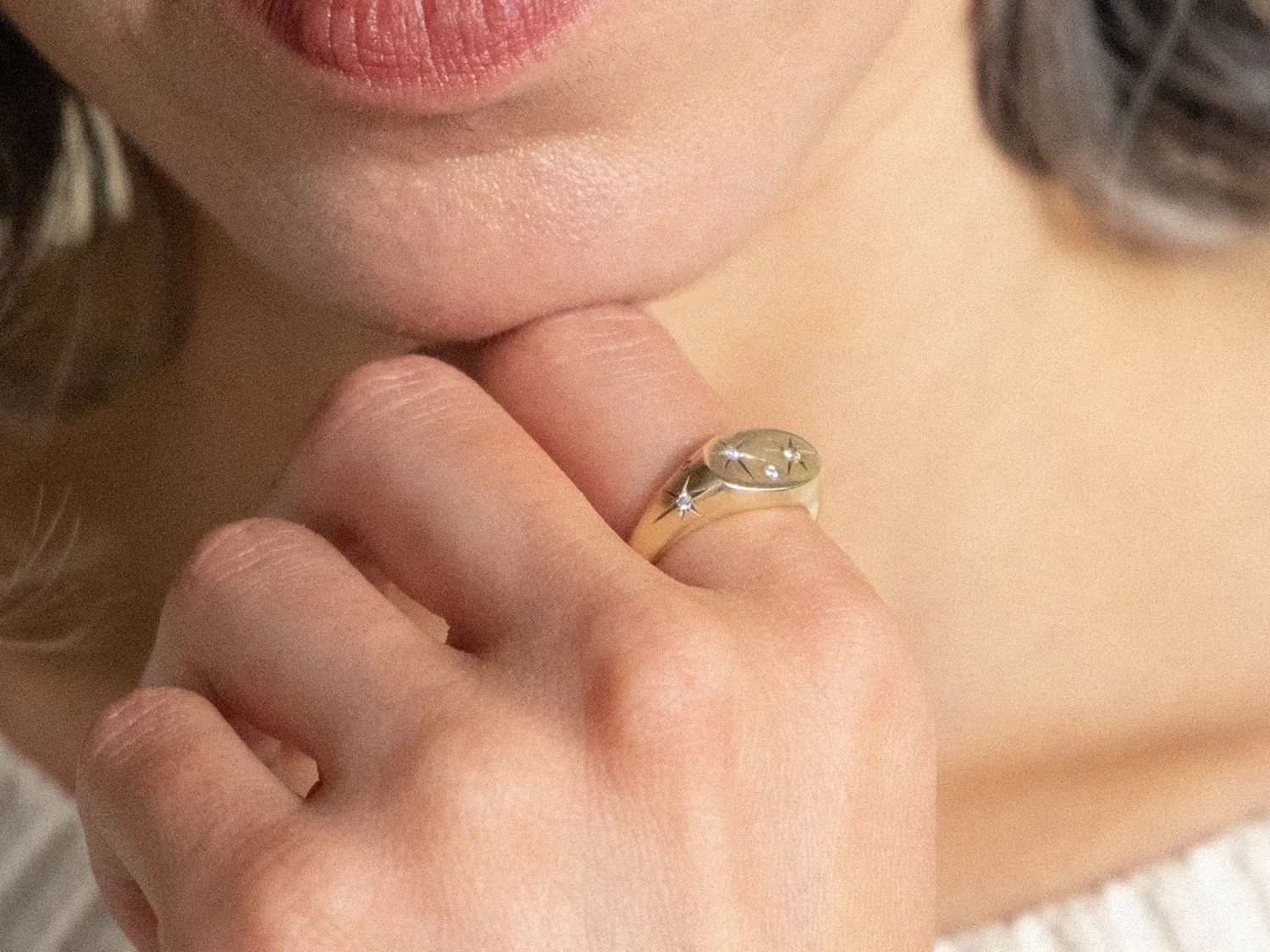 Close up of a model's hand with a chunky gold signet ring set with diamonds and engraved stars