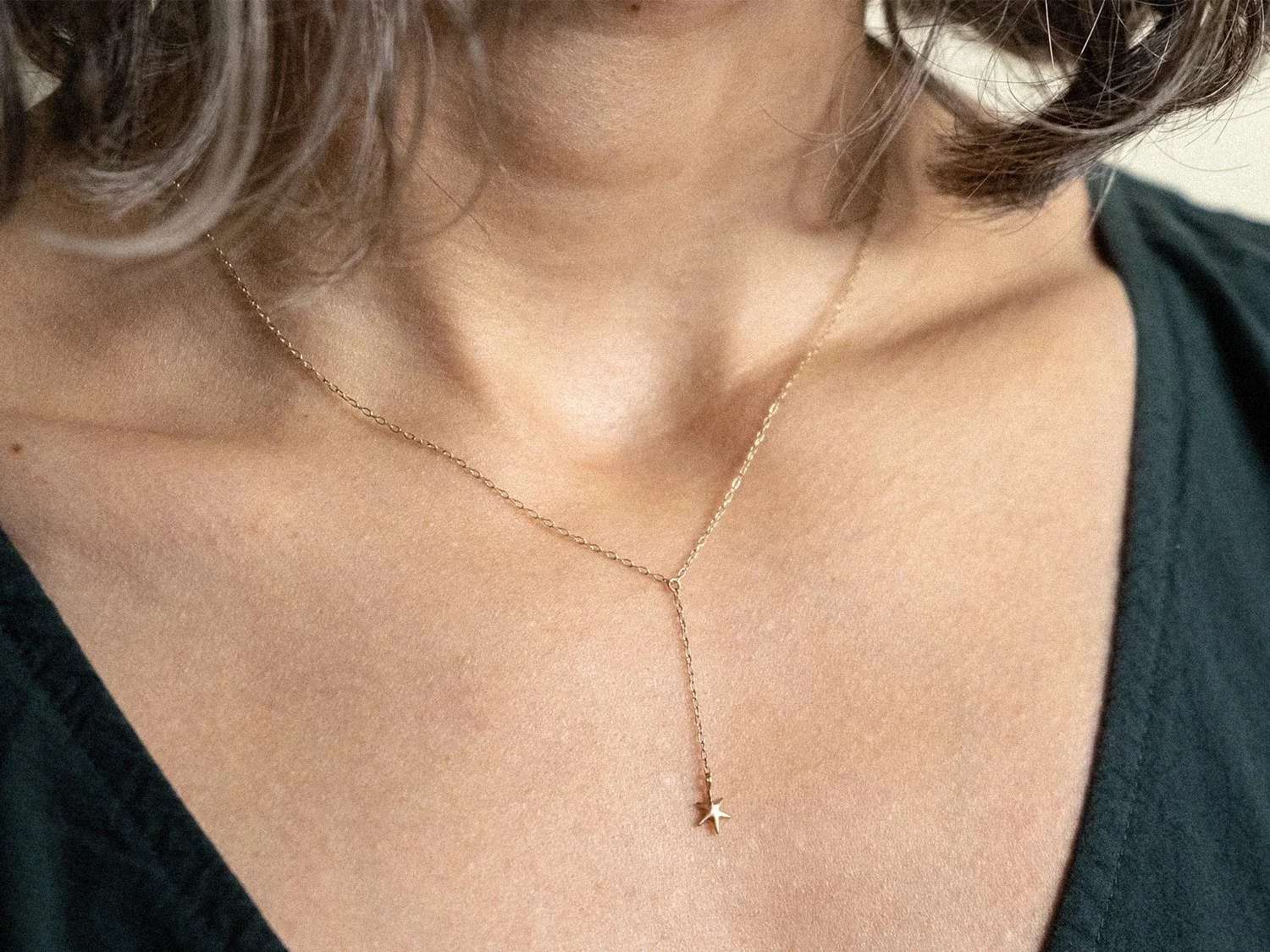 Close up on female model wearing a delicate gold chain necklace with a hanging star