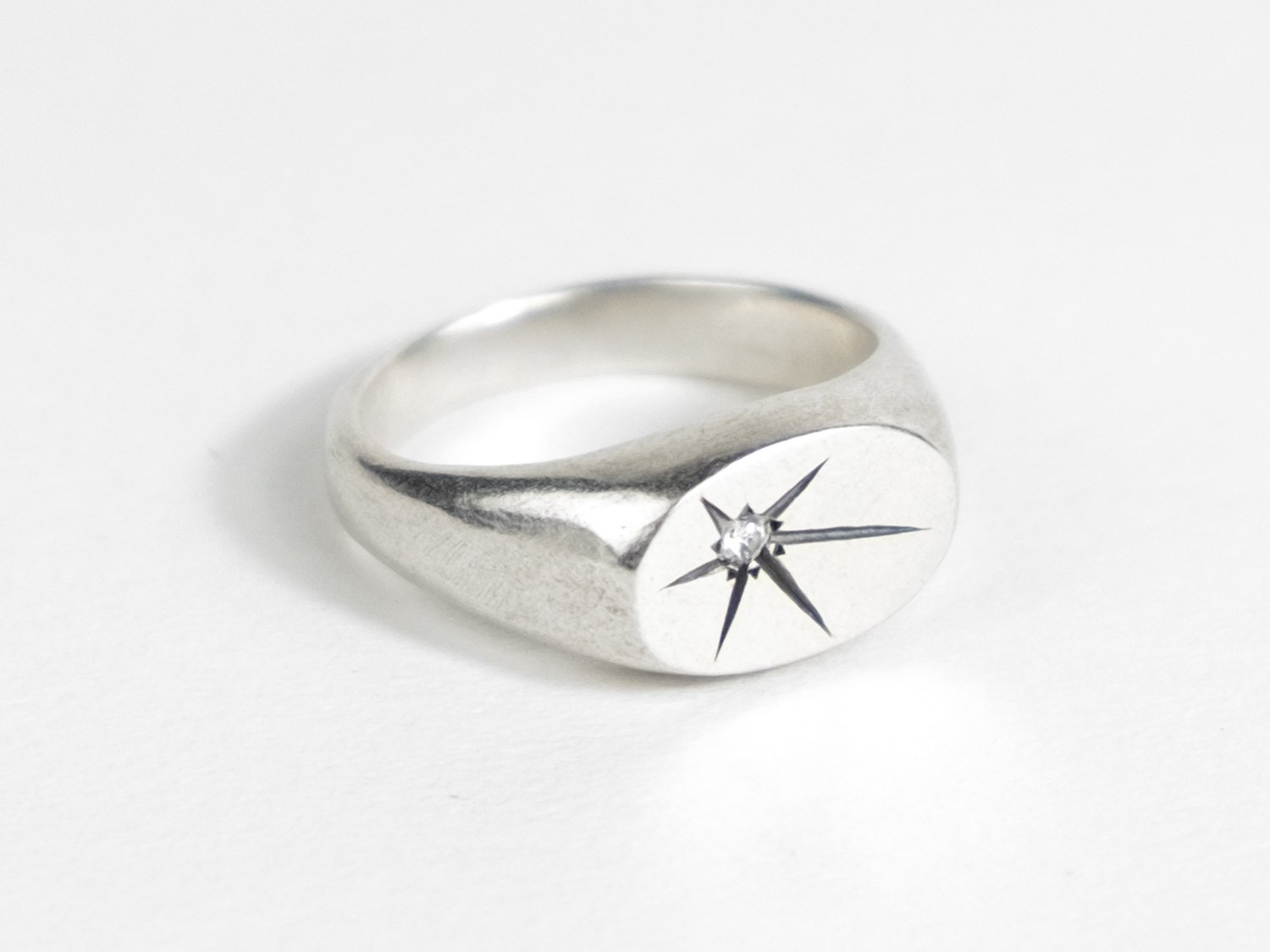 Wide silver signet ring with a single star-set diamond on the flat face