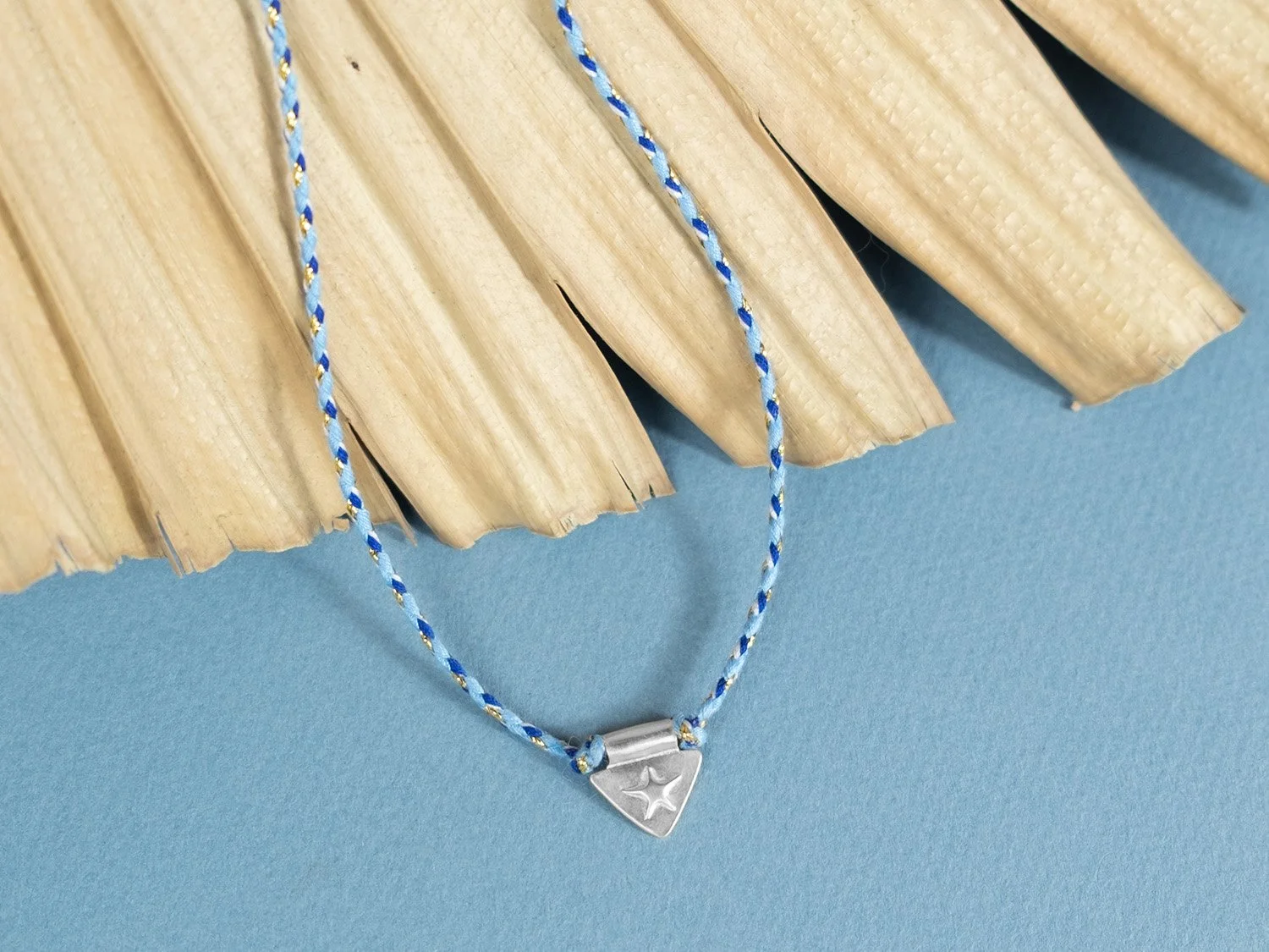 Triangle-shaped silver charm with a raised star on blue braided cord