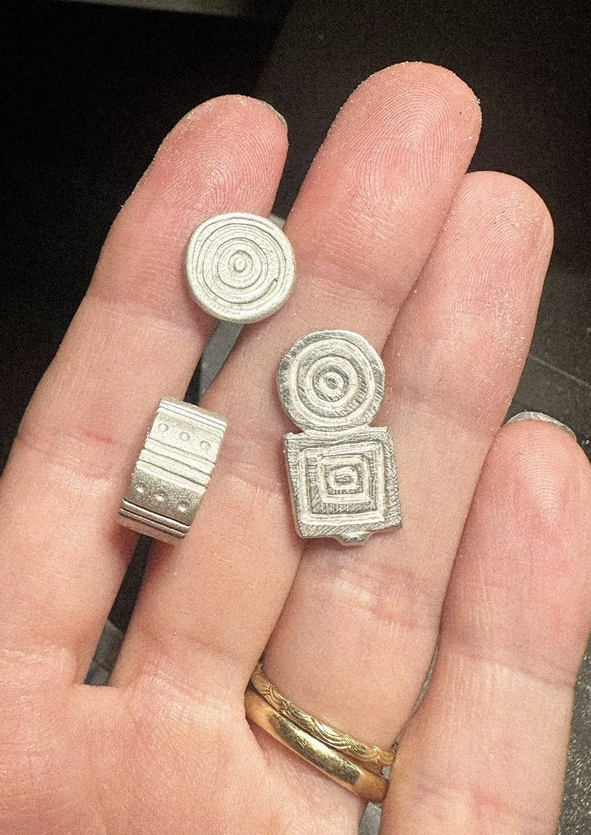 A hand holding silver shapes and hoop earrings