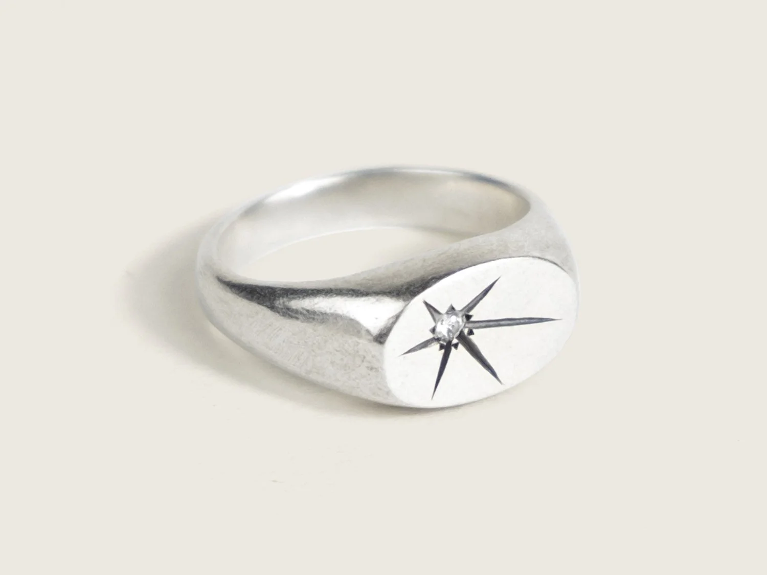 Wide silver signet ring with a single star-set diamond on the flat face