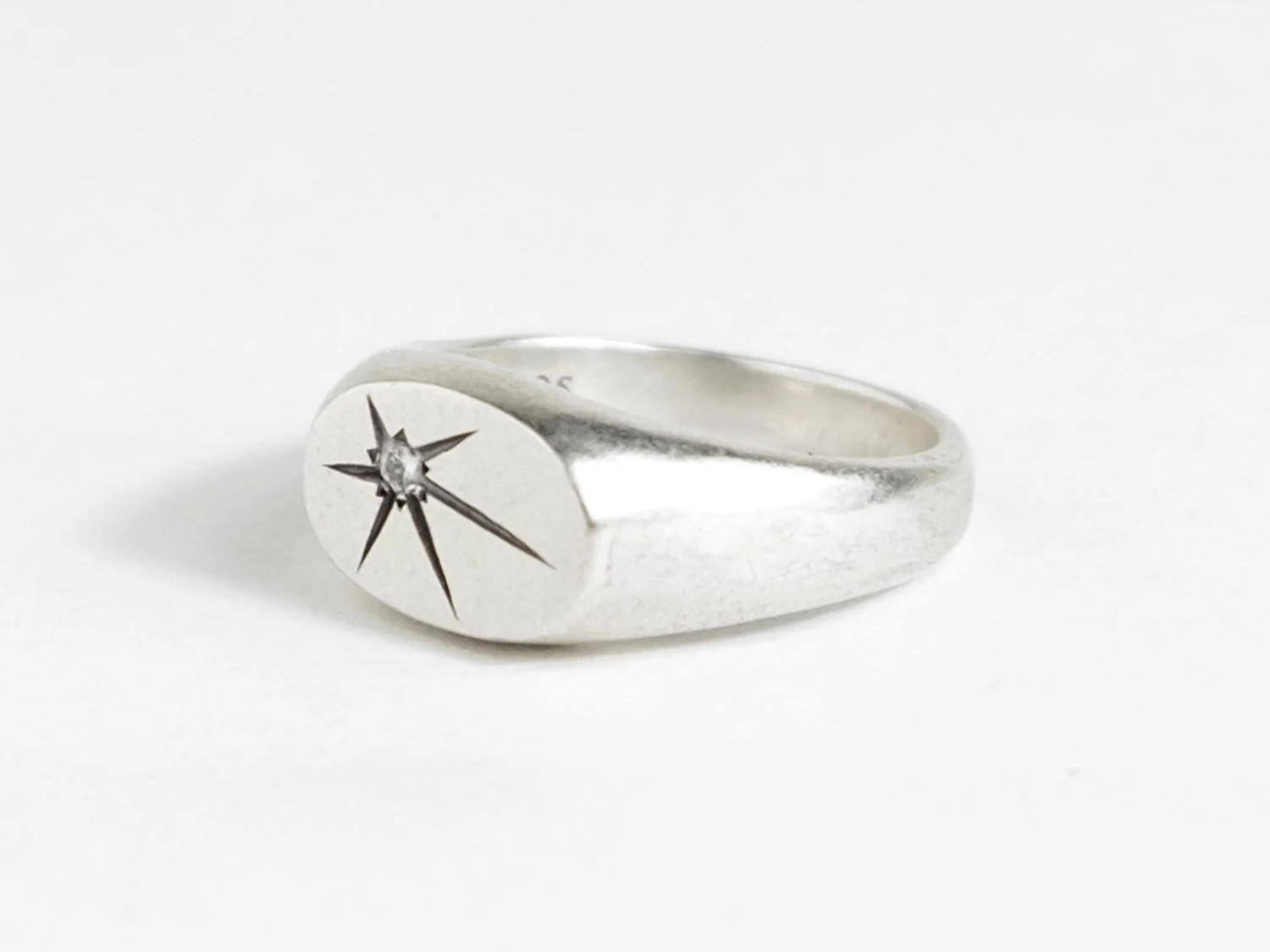 Wide silver signet ring with a single star-set diamond on the flat face