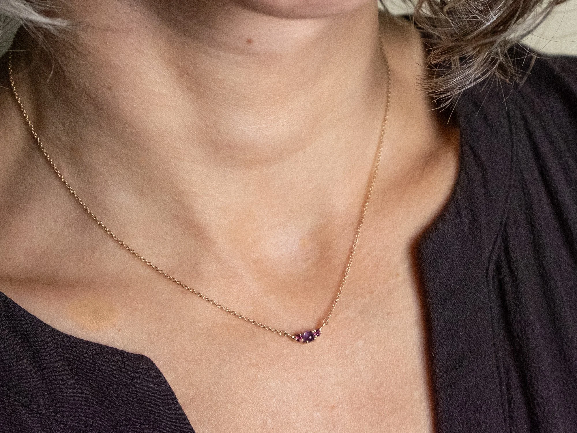 Close up of a model wearing a gold necklace with round amethyst and garnet stones in the center