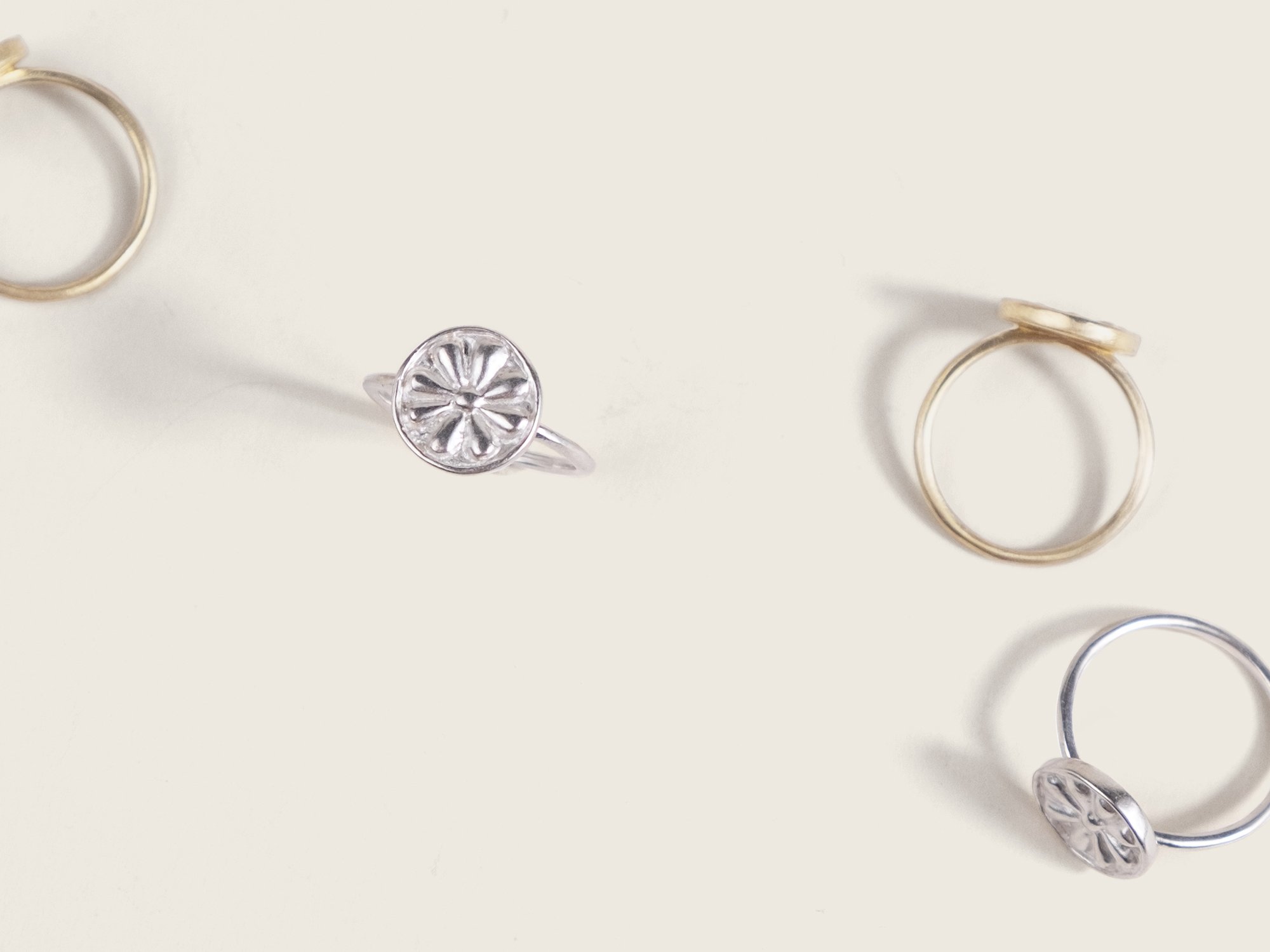 The same ring in gold and silver with a floral motif on top, scattered across a surface