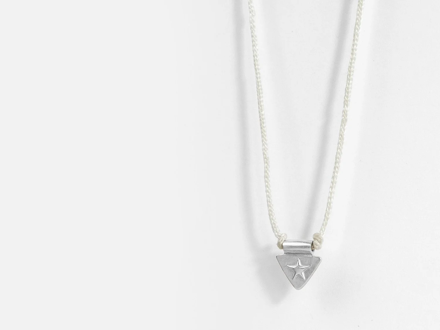 Triangle-shaped silver charm with a raised star on ivory braided cord