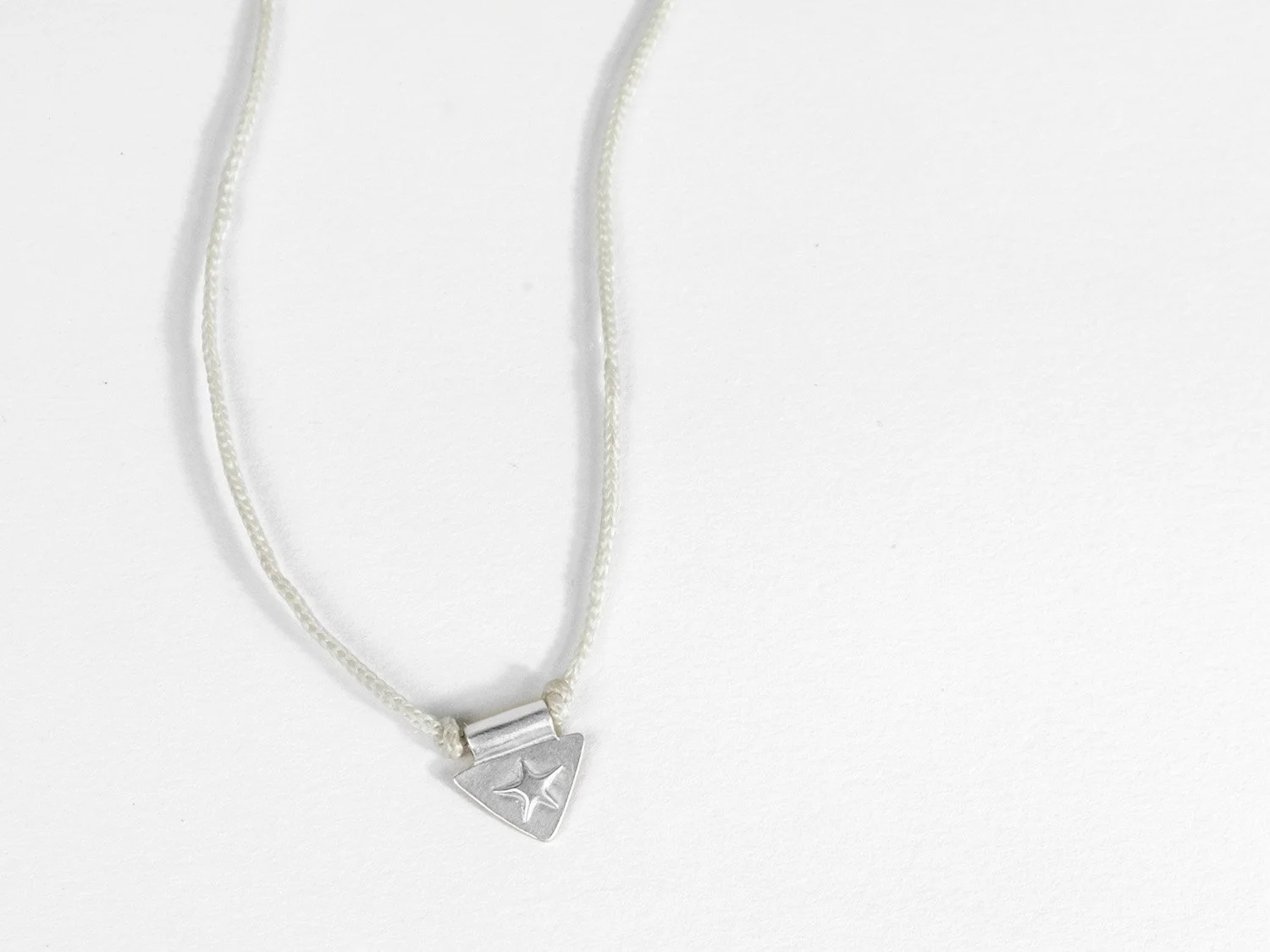 Triangle-shaped silver charm with a raised star on ivory braided cord