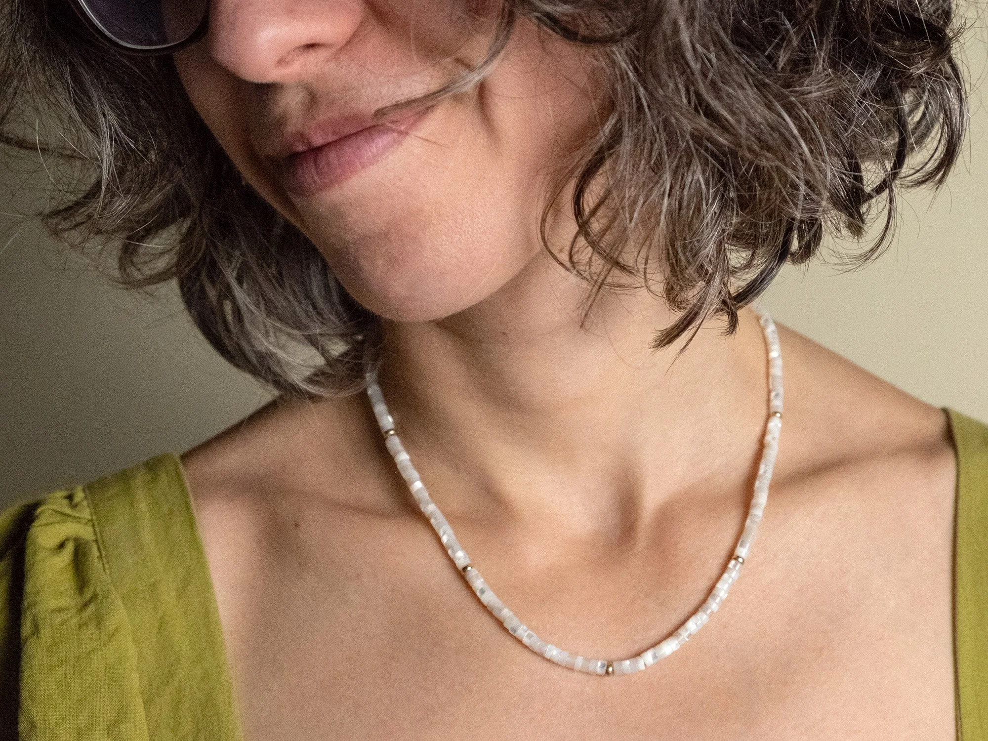 Close up of a female model wearing a beaded mother-of-pearl necklace with gold beads