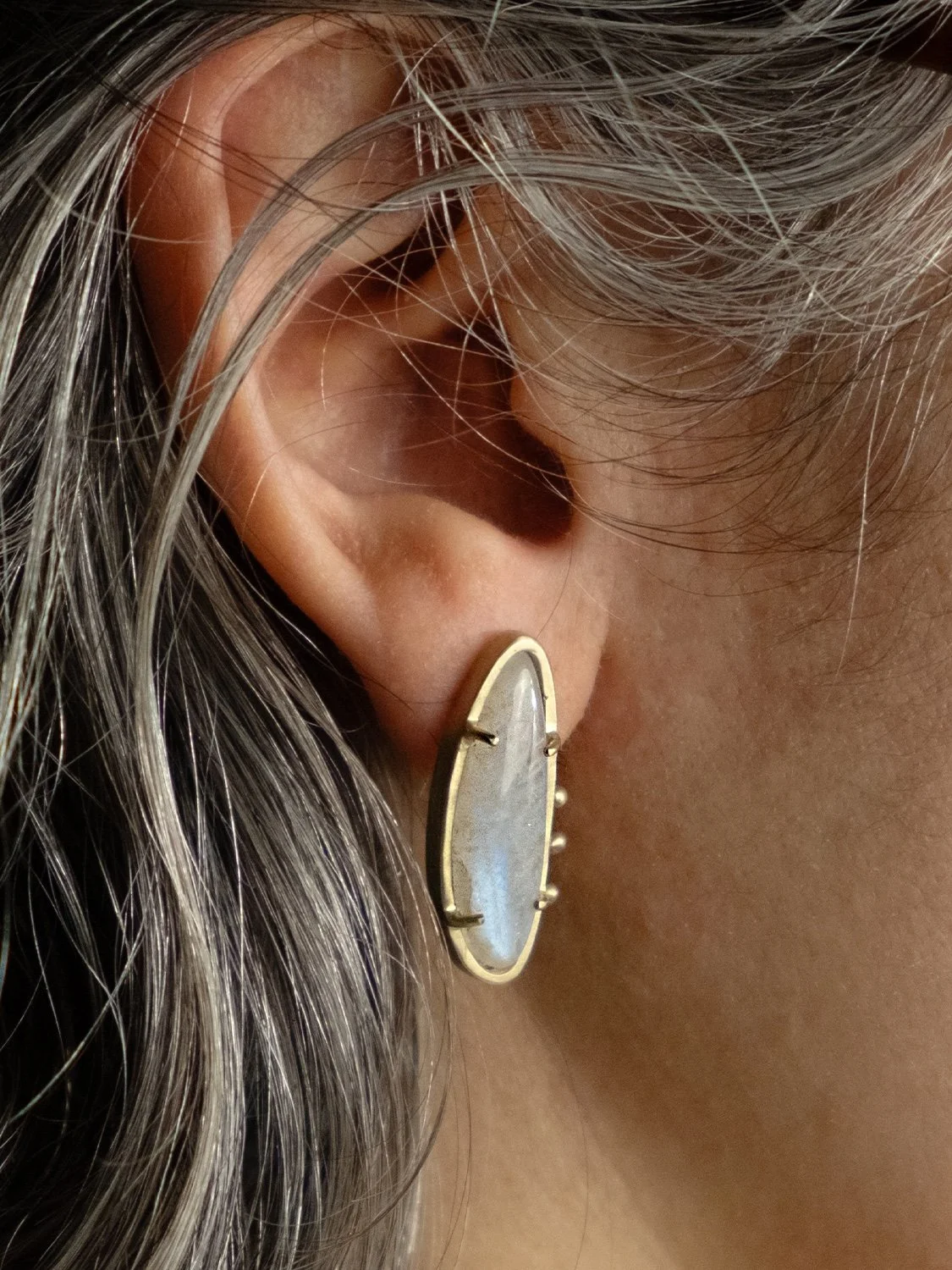 Close up of a female model wearing 14k gold and moonstone stud earrings by Sara Golden Jewelry