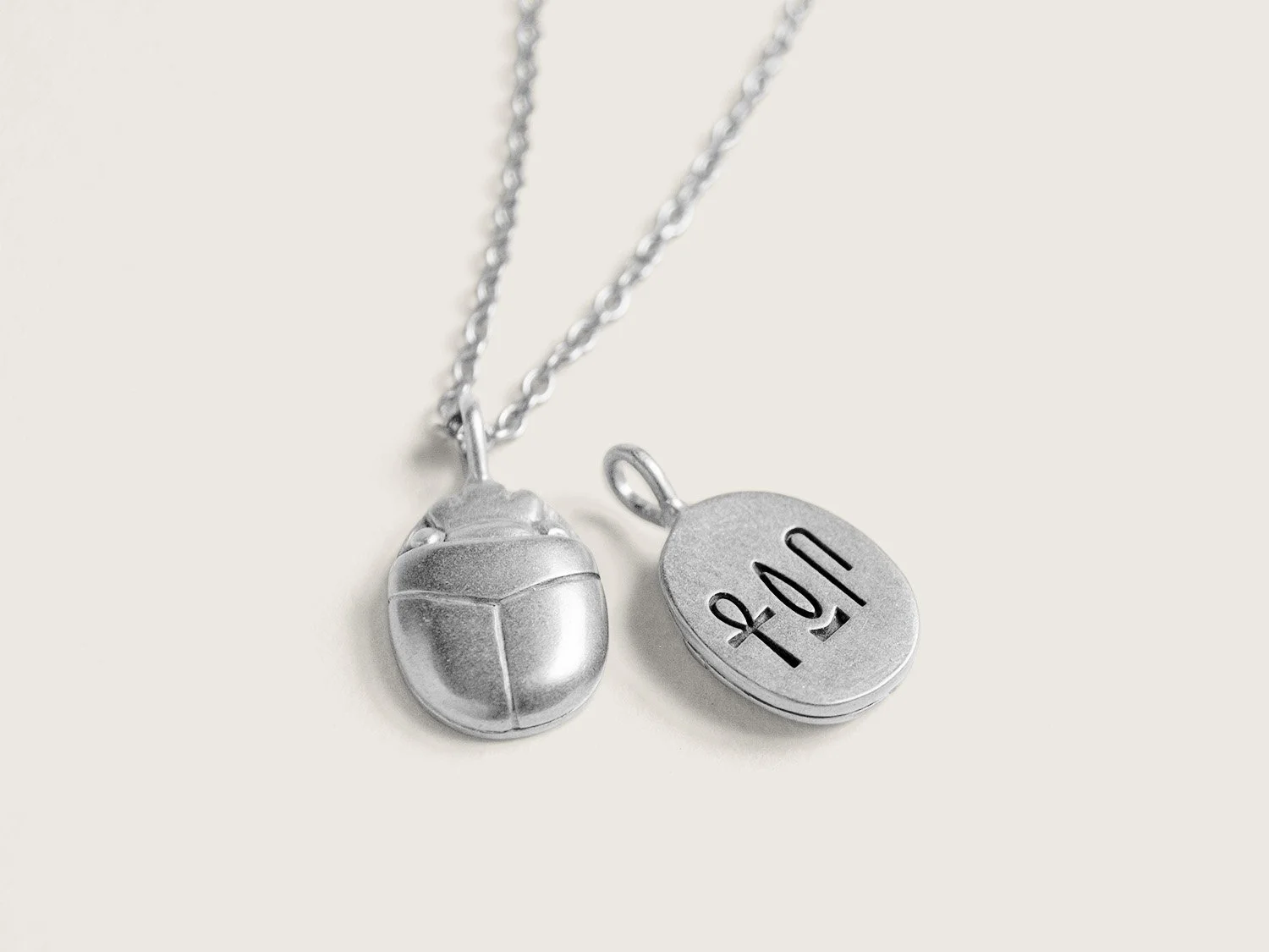 Silver pendant necklace in the shape of a scarab beetle with hieroglyphs carved into the back