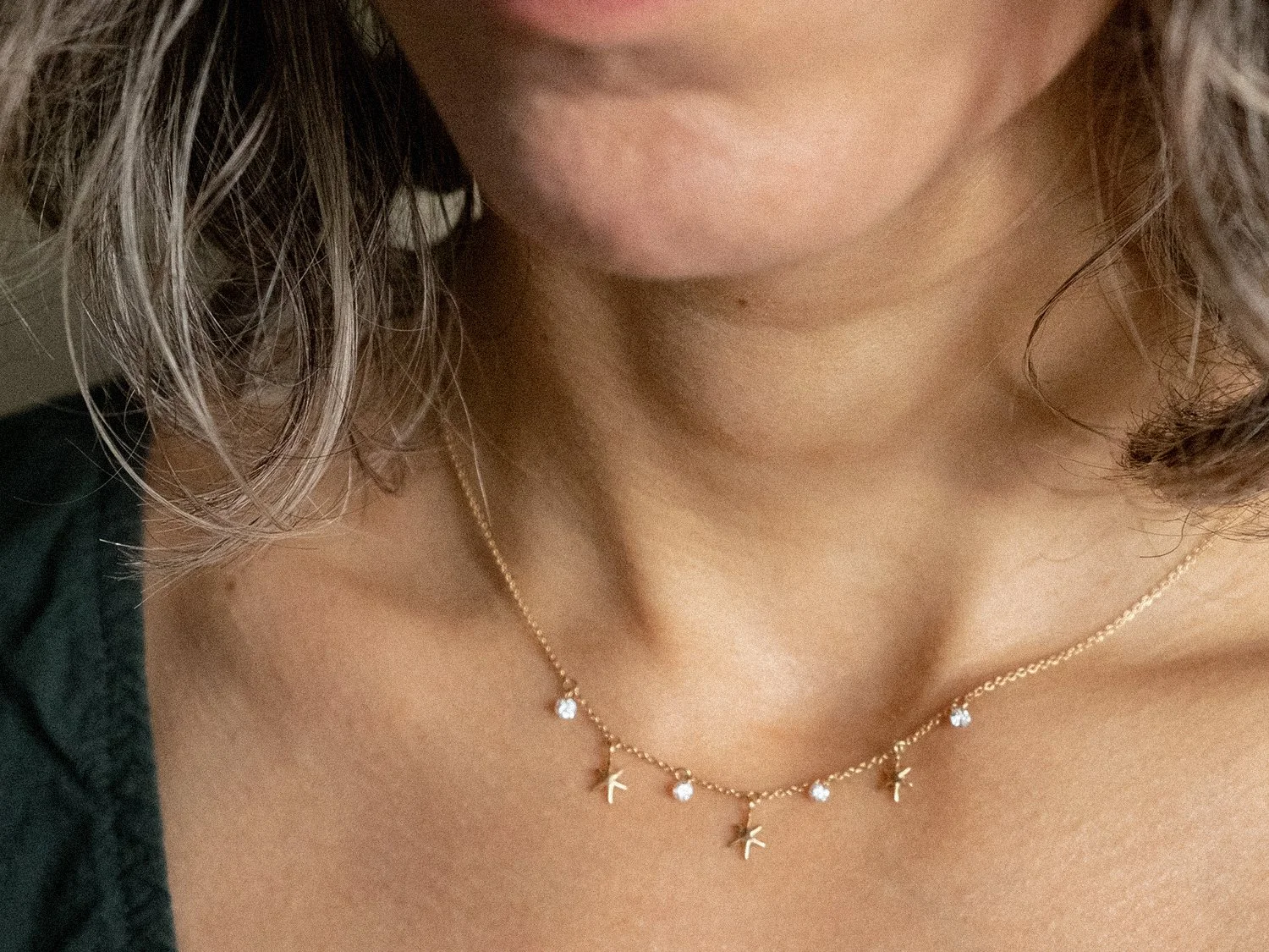 Close up of a model wearing a delicate gold chain neckalce with hanging stars and diamonds