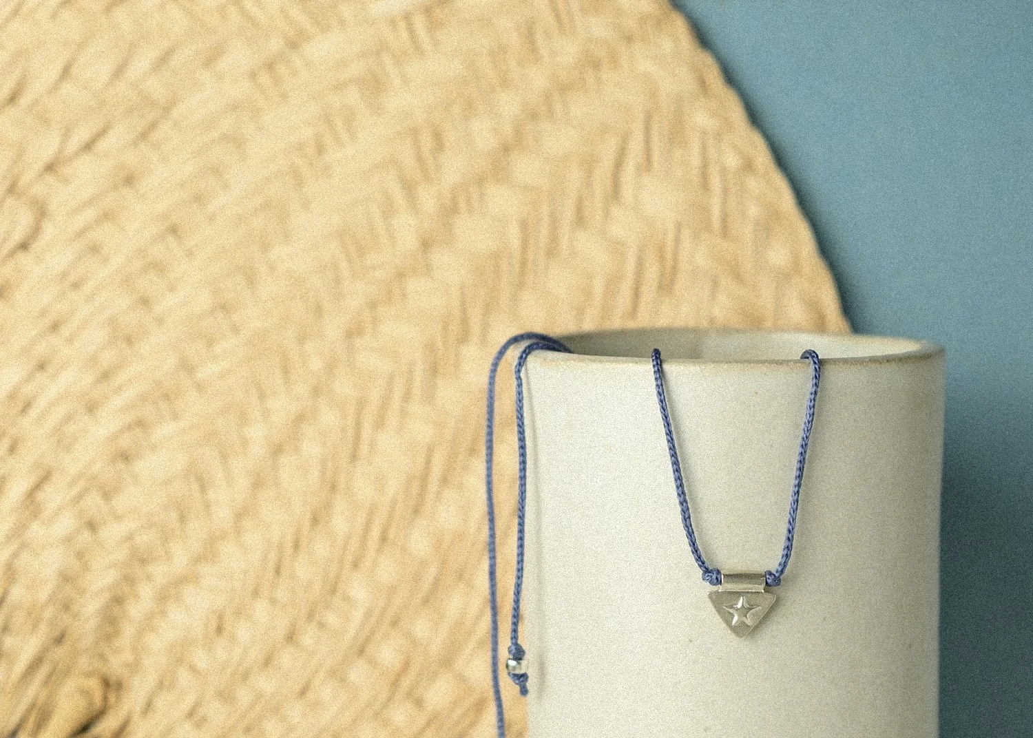 Silver triangle and star charm necklace on a blue cord coming out of a ceramic dish