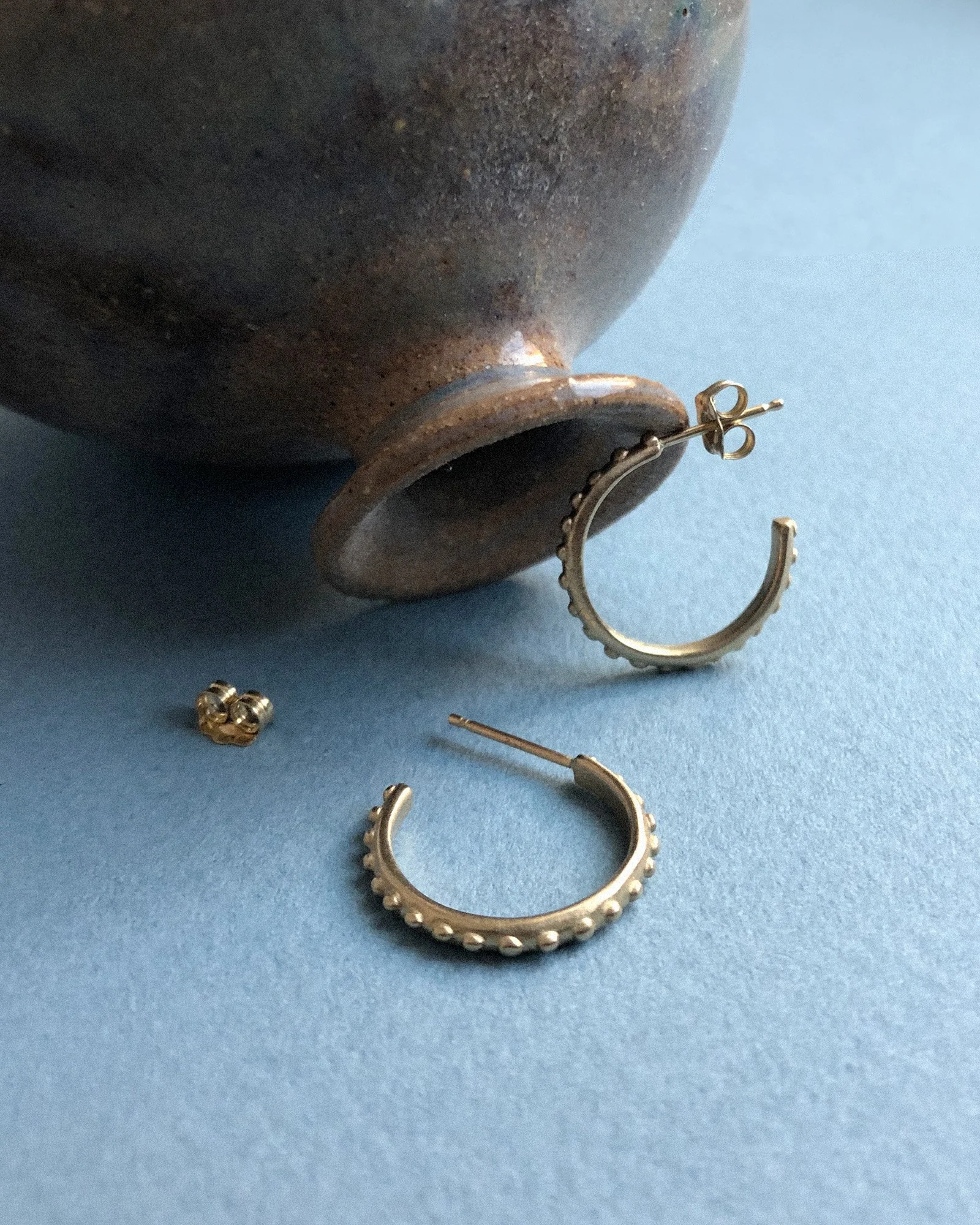 Small gold hoop earrings resting against a ceramic vessel